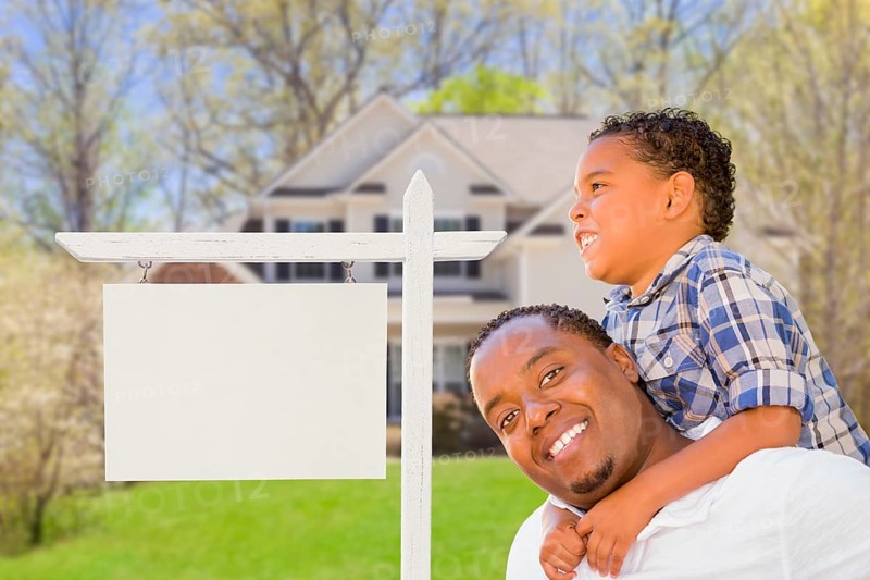 Happy african american father and mixed-race son in front of blank real estate sign and new house