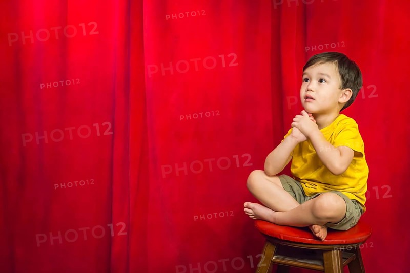 Handsome mixed-race boy sitting on stool in front of red curtain
