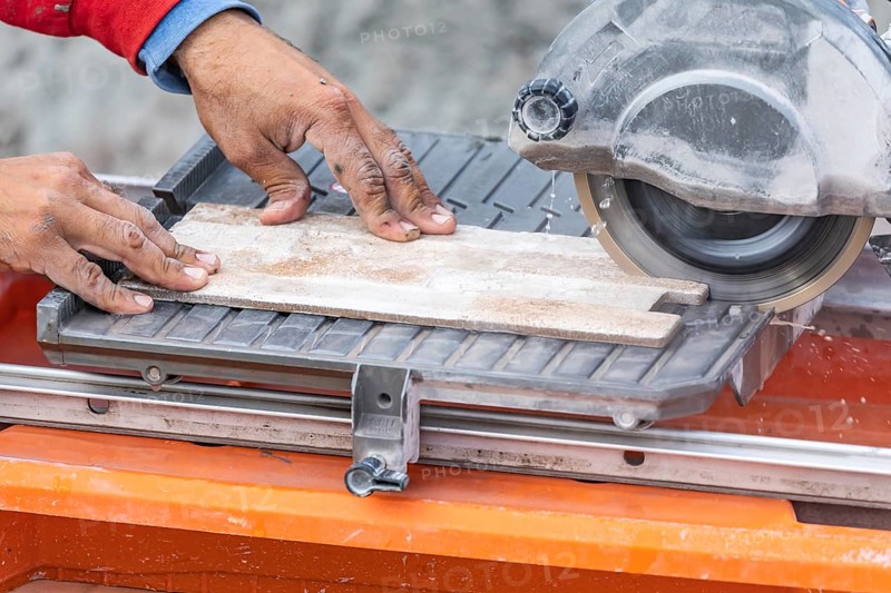 Worker using wet tile saw to cut wall tile at construction site