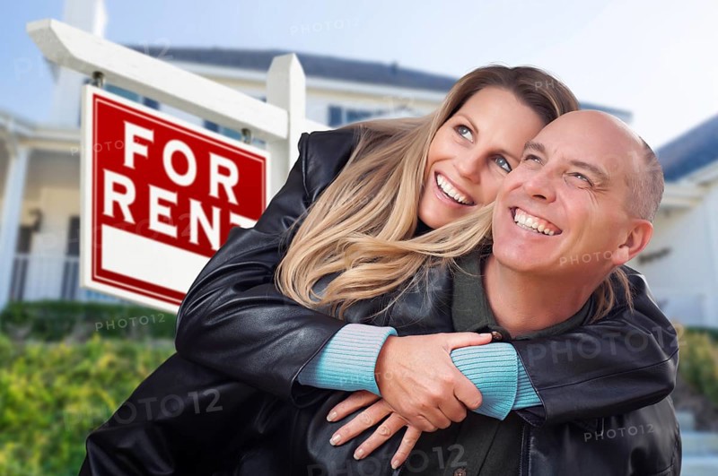 Happy couple hugging in front of for rent real estate sign and house
