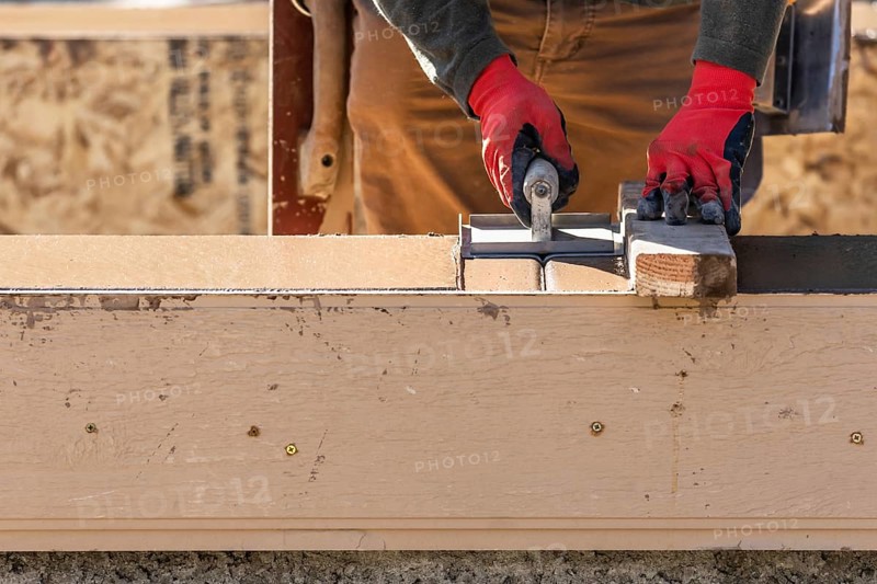 Construction worker using hand groover on wet cement forming coping around new pool