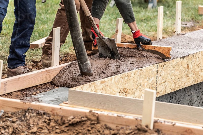 Construction workers pouring and leveling wet cement into wood framing