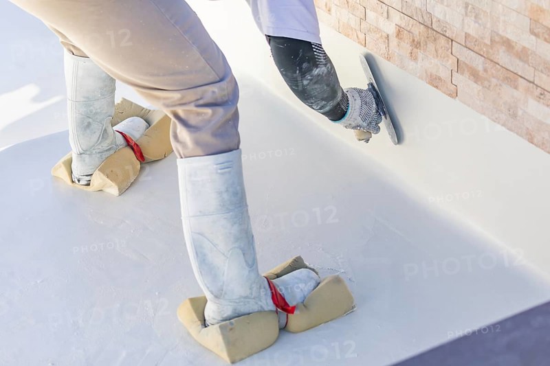 Worker wearing sponges on shoes smoothing wet pool plaster with trowel