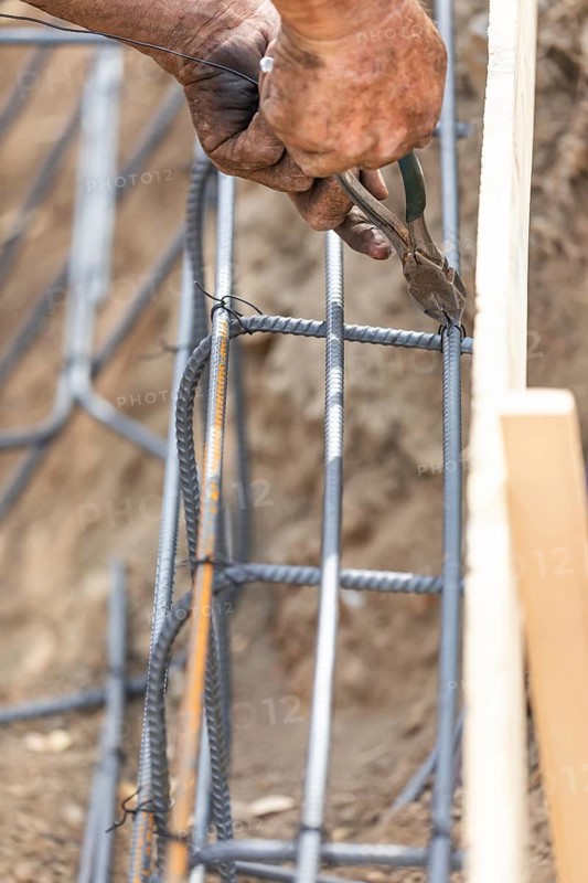 Worker securing steel rebar framing with wire plier cutter tool at construction site