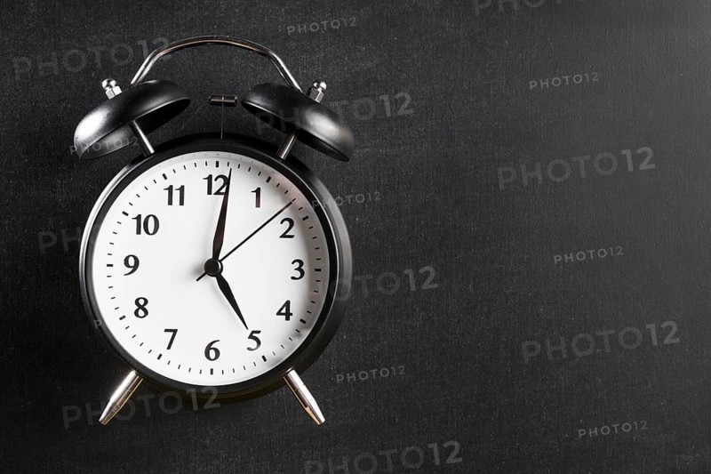 Alarm clock showing 5 o clock against black background