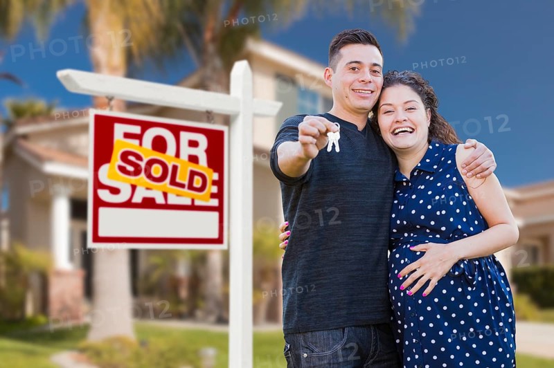 Young happy pregnant hispanic young couple with house keys in front of their new home and sold for sale real estate sign