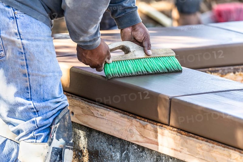 Construction worker using brush on wet cement forming coping around new pool