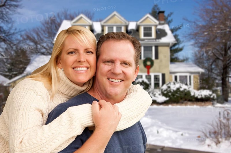 Happy couple in front of beautiful house with snow on the ground