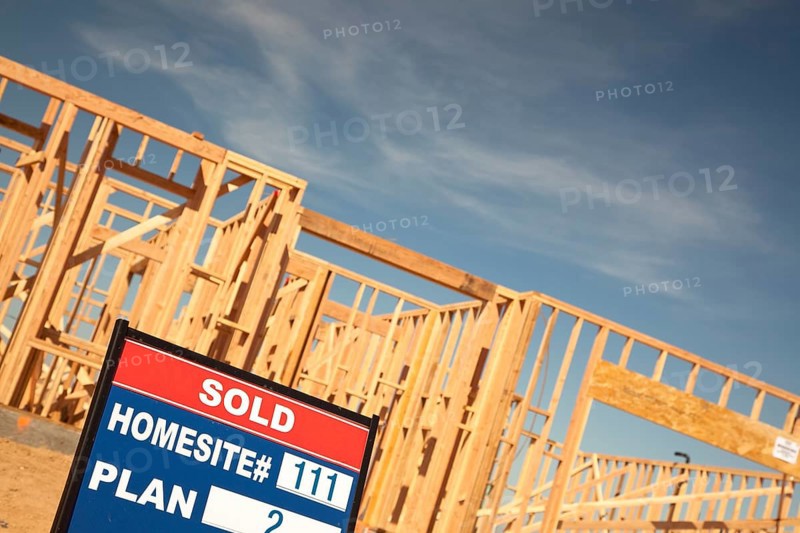 Sold lot real estate sign at new home framing construction site against deep blue sky