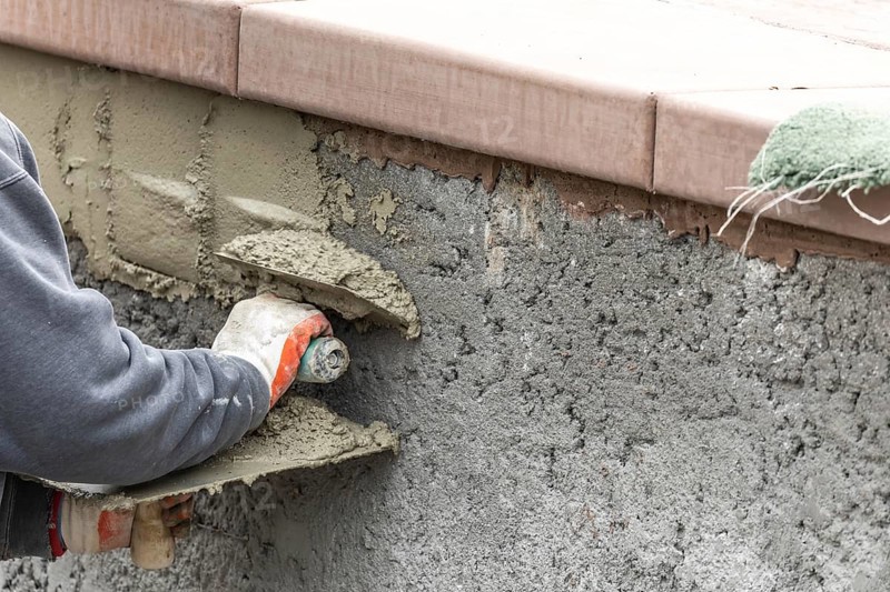 Tile worker applying cement with trowel at pool construction site