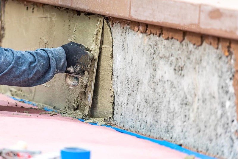 Tile worker applying cement with trowel at pool construction site