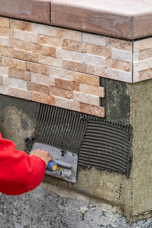 Worker installing wall tile cement with trowel and tile at construction site