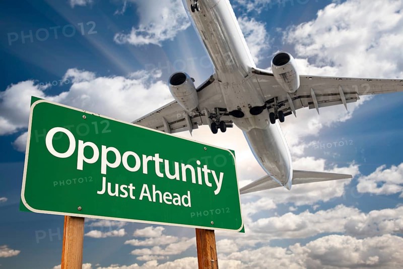 Opportunity green road sign and airplane above with dramatic blue sky and clouds
