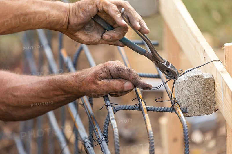 Worker securing steel rebar framing with wire plier cutter tool at construction site