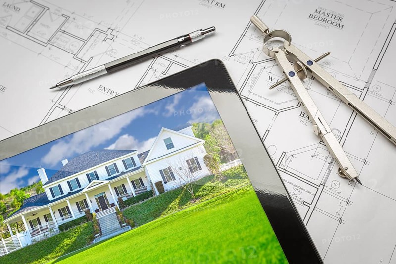 Computer tablet showing finished house sitting on house plans with pencil and compass