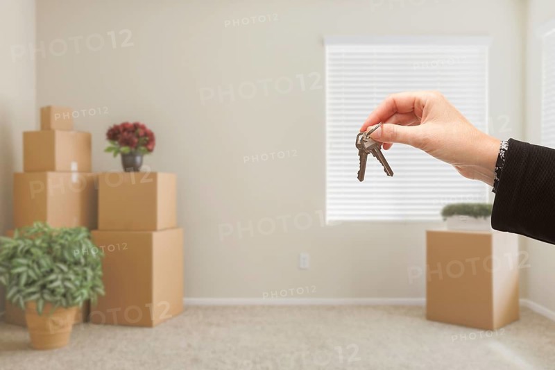 Woman handing over house keys in room with packed moving boxes