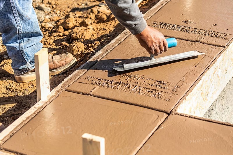 Construction worker using trowel on wet cement forming coping around new pool