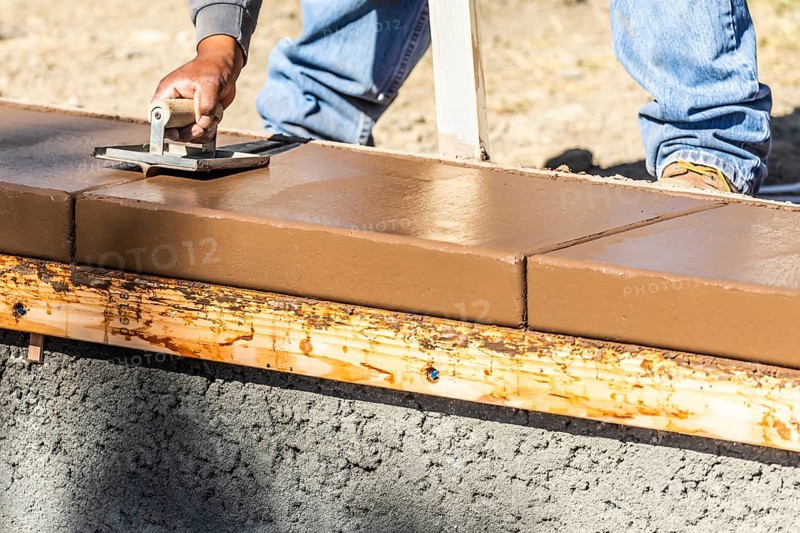 Construction worker using hand groover on wet cement forming coping around new pool