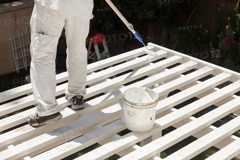 Painter rolling white paint onto the top of A home patio cover