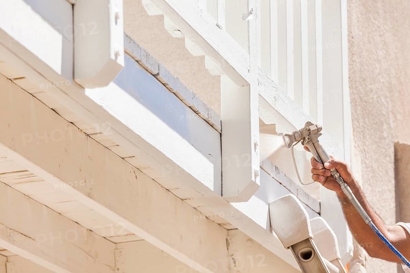 House painter wearing facial protection spray painting A deck of A home