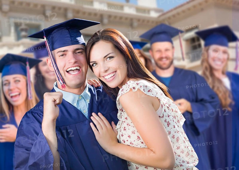 Proud male graduate in cap and gown with girl among other graduates behind