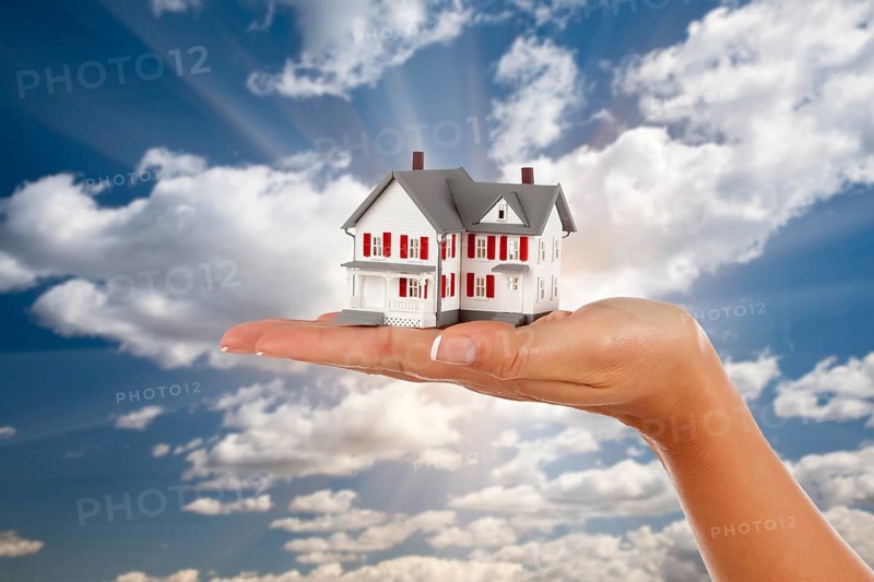 Model house in female hand on a cloud and sky background