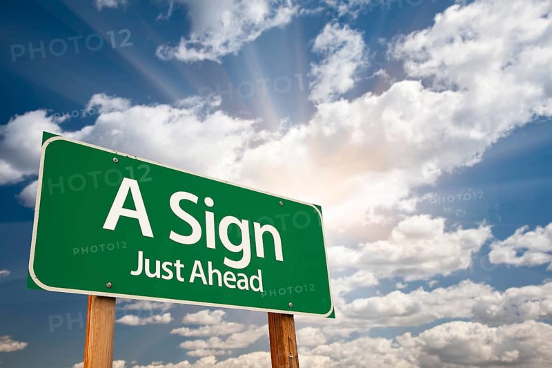 A sign green road sign against clouds and sunburst