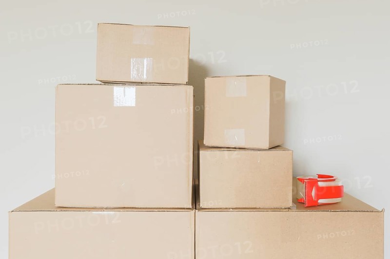 Variety of packed moving boxes and tape gun in empty room against wall