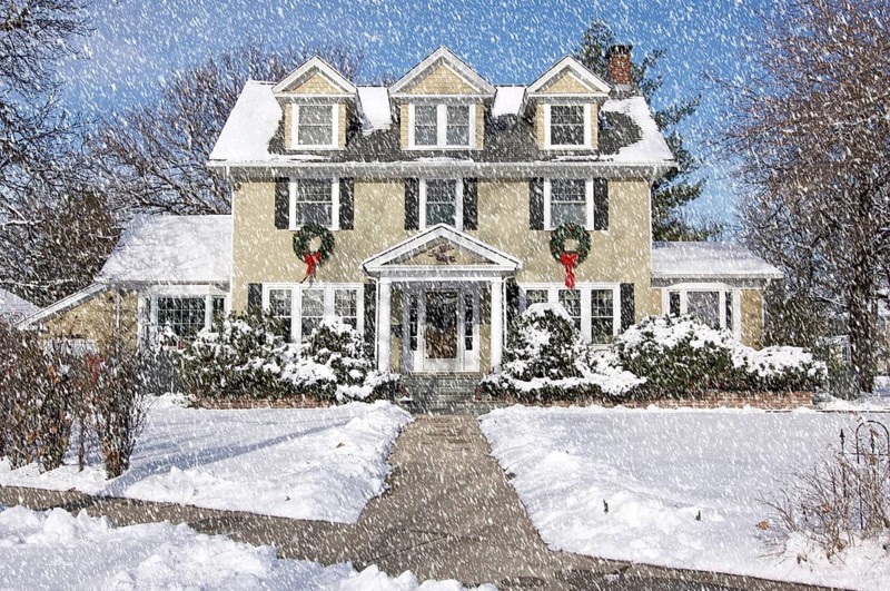 Majestic newly constructed home facade with giant christmas wreaths on a snowing blustery day