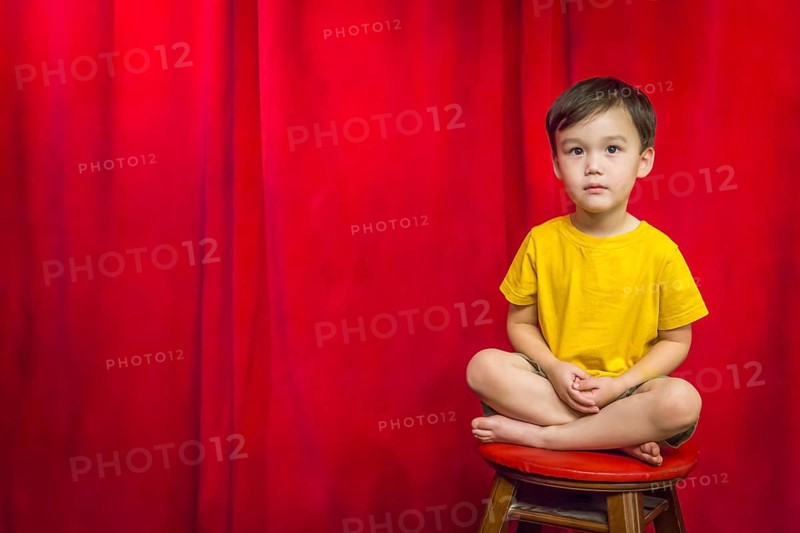 Handsome mixed-race boy sitting on stool in front of red curtain