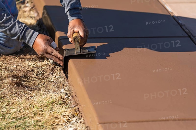 Construction worker smoothing wet cement with curb tool