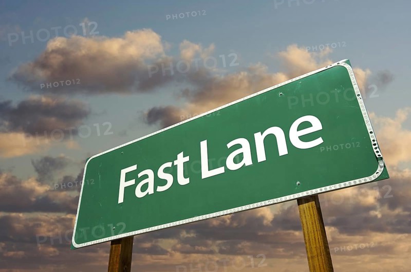 Fast lane green road sign over dramatic clouds and sky