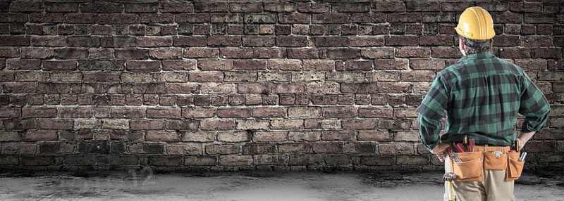 Contractor wearing hard hat and tool belt facing blank old brick wall banner with copy space
