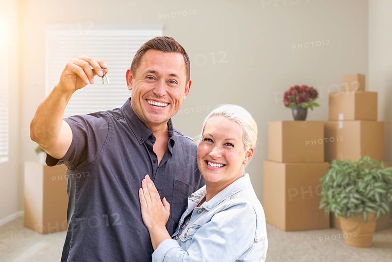Happy couple with new house keys inside empty room with boxes