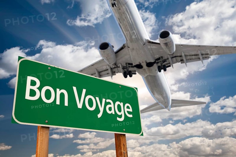 Bon voyage green road sign and airplane above with dramatic blue sky and clouds