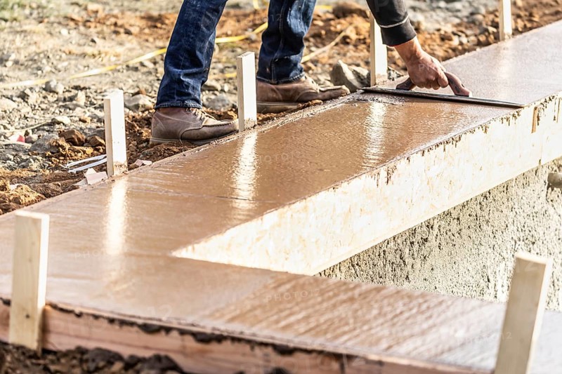 Construction worker using wood trowel on wet cement forming coping around new pool