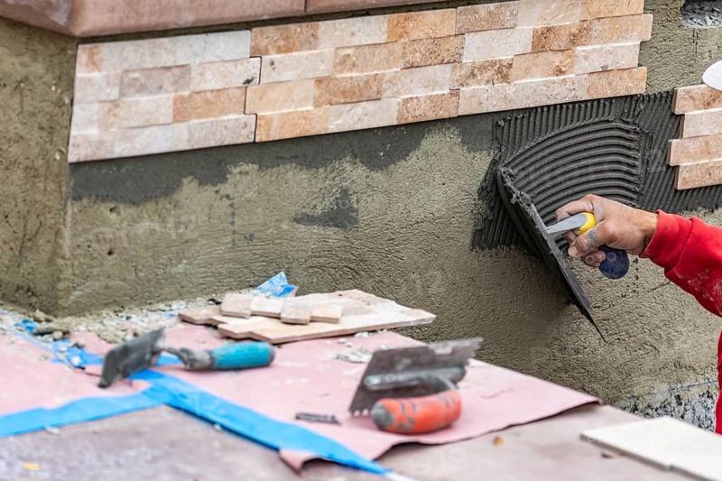 Worker installing wall tile cement with trowel and tile at construction site