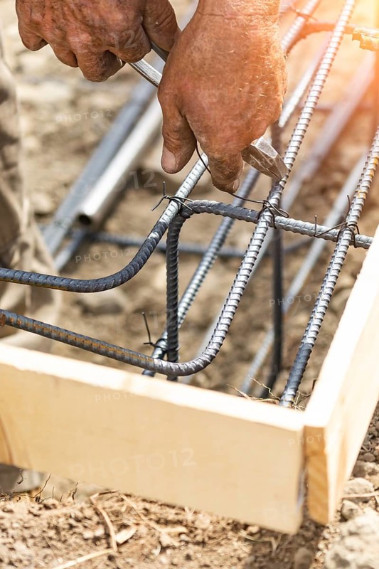 Worker securing steel rebar framing with wire plier cutter tool at construction site