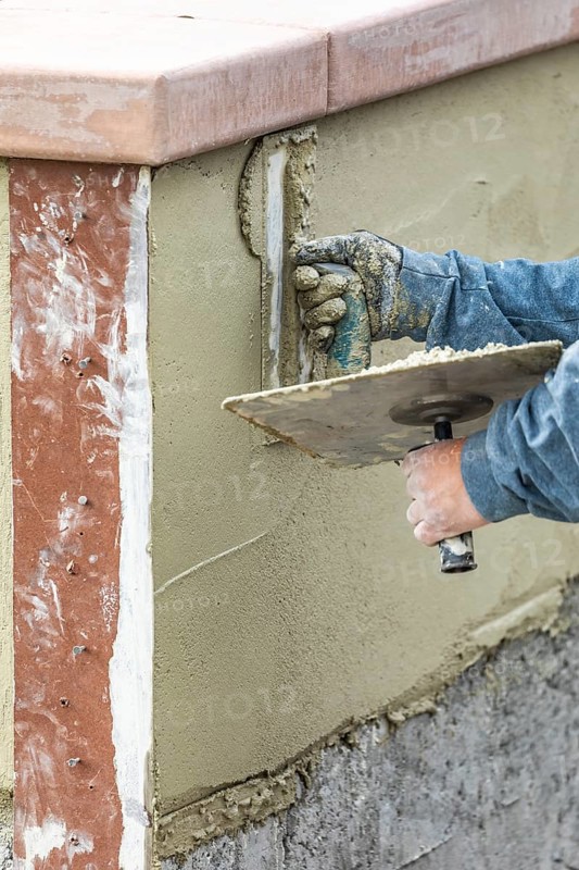 Tile worker applying cement with trowel at pool construction site