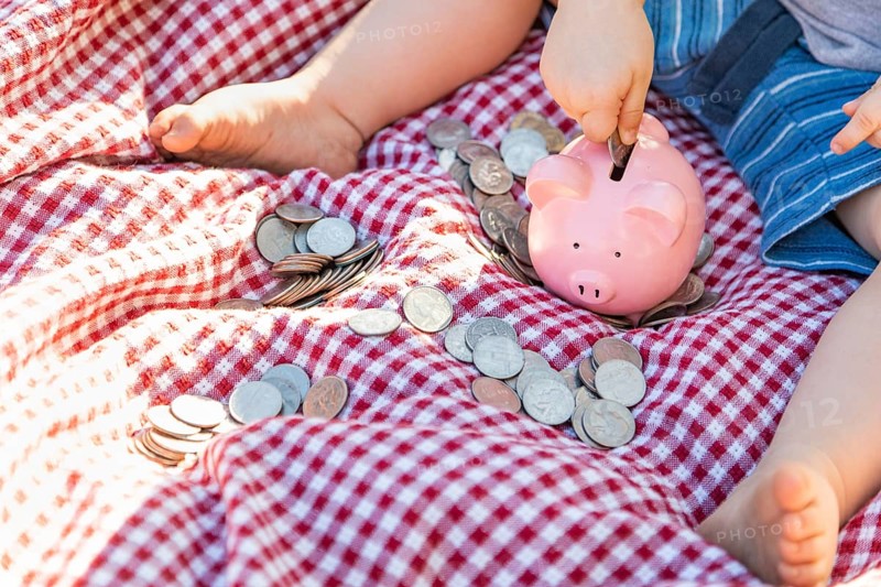 Baby boy sitting on picnic blanket putting coins in piggy bank