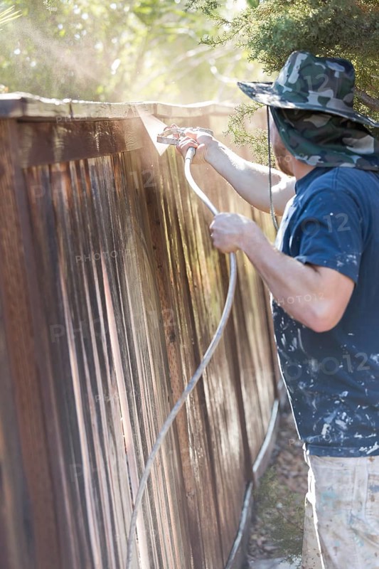 Professional painter spraying house yard fence with wood stain