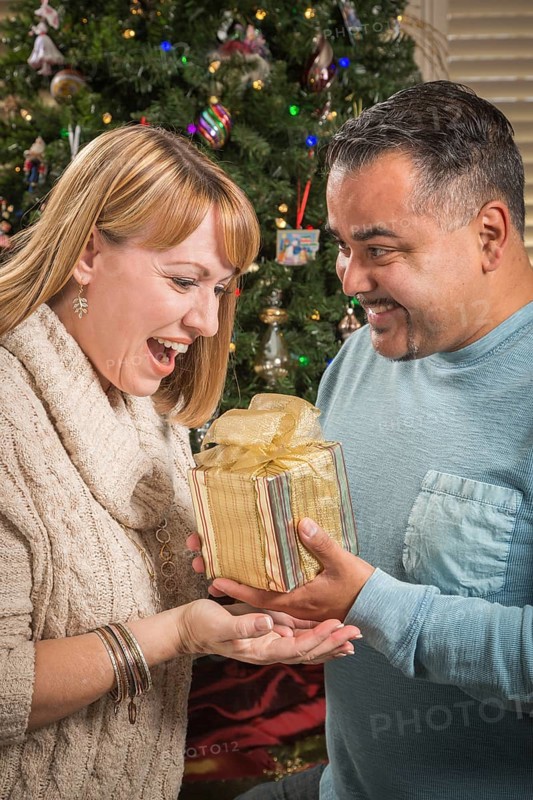 Happy young mixed-race couple with present near christmas tree
