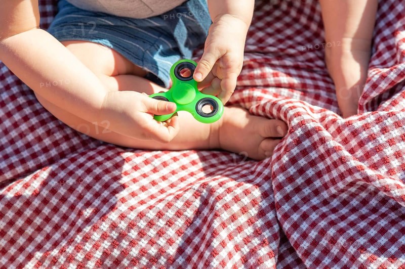 Baby boy sitting on picnic blanket playing with fidget spinner