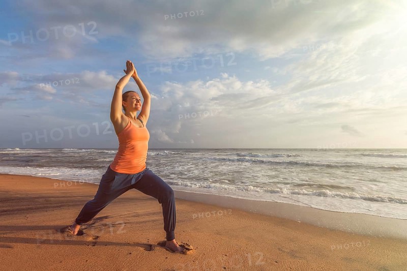 Woman doing Hatha yoga asana Virabhadrasana 1 Warrior Pose outdoors on ocean beach on sunset. Kerala