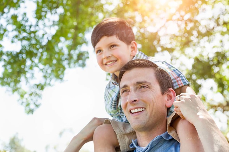 mixed-race father and son playing piggyback together in the park