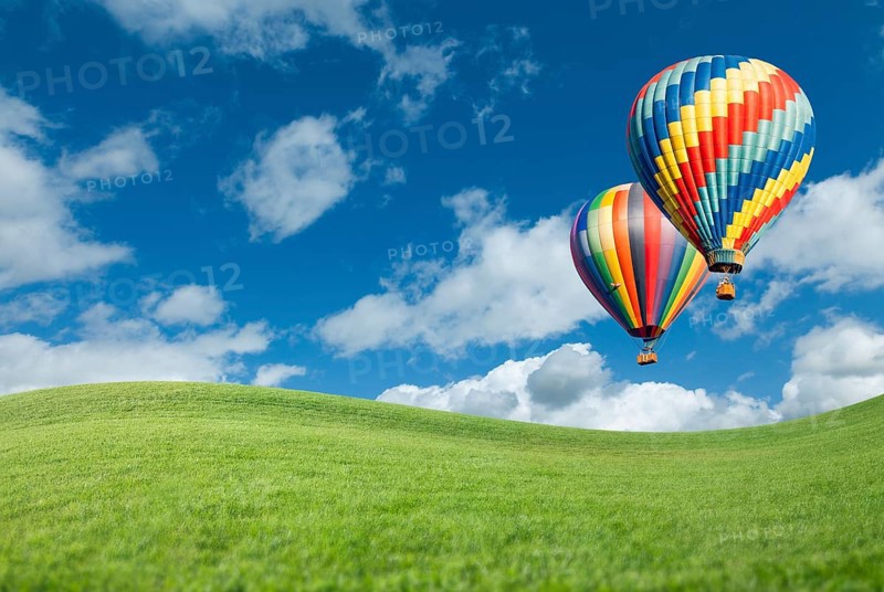 Two hot air balloons up in the beautiful blue sky with grass field below