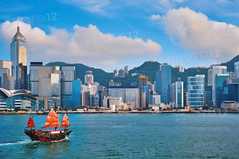 Hong Kong skyline cityscape downtown skyscrapers over Victoria Harbour in the evening with junk tourist ferry boat on sunset with dramatic sky Hong Kong