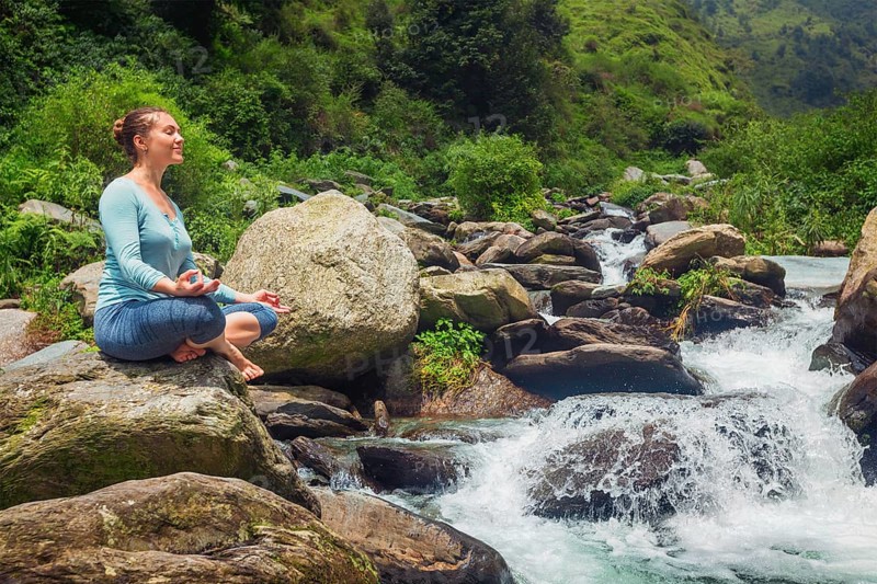 Woman doing yoga meditation asana Padmasana lotus pose outdoors at tropical waterfall