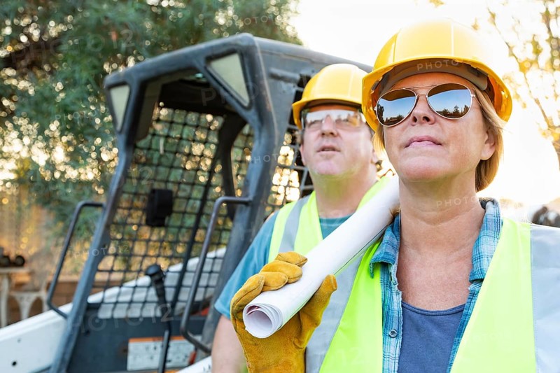 Male and female workers with technical blueprints at construction site