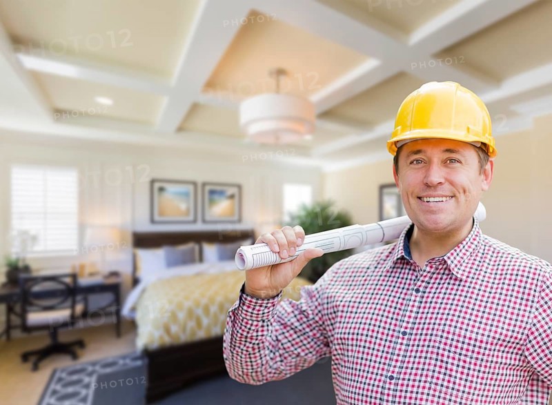 Smiling contractor in hard hat with roll of plans over custom bedroom drawing and photo combination
